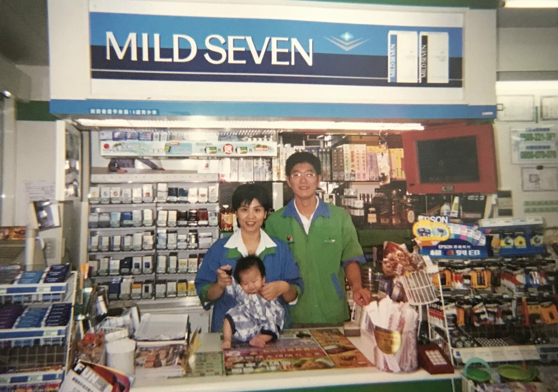 A photograph of a family of three standing behind a convenience store counter