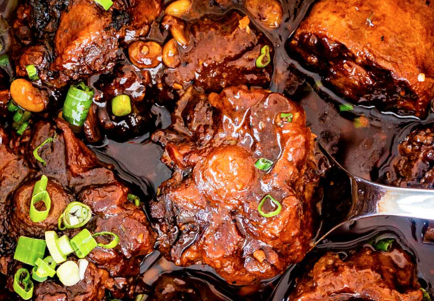 A closeup photograph of Jamaican oxtail in a rich gelatin with green onion