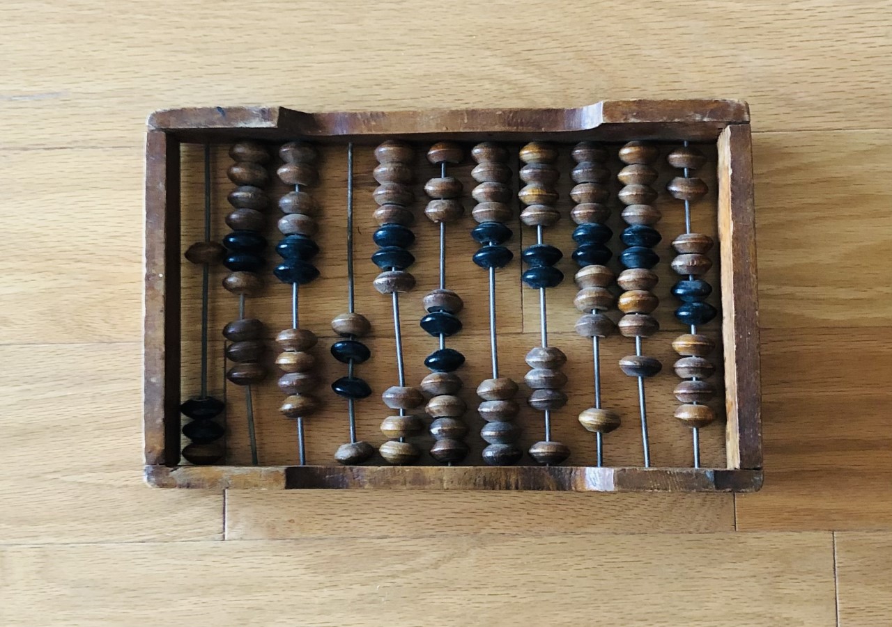 Picture of an abacus, with rows of brown and black beads that slide in grooves on a flat surface.